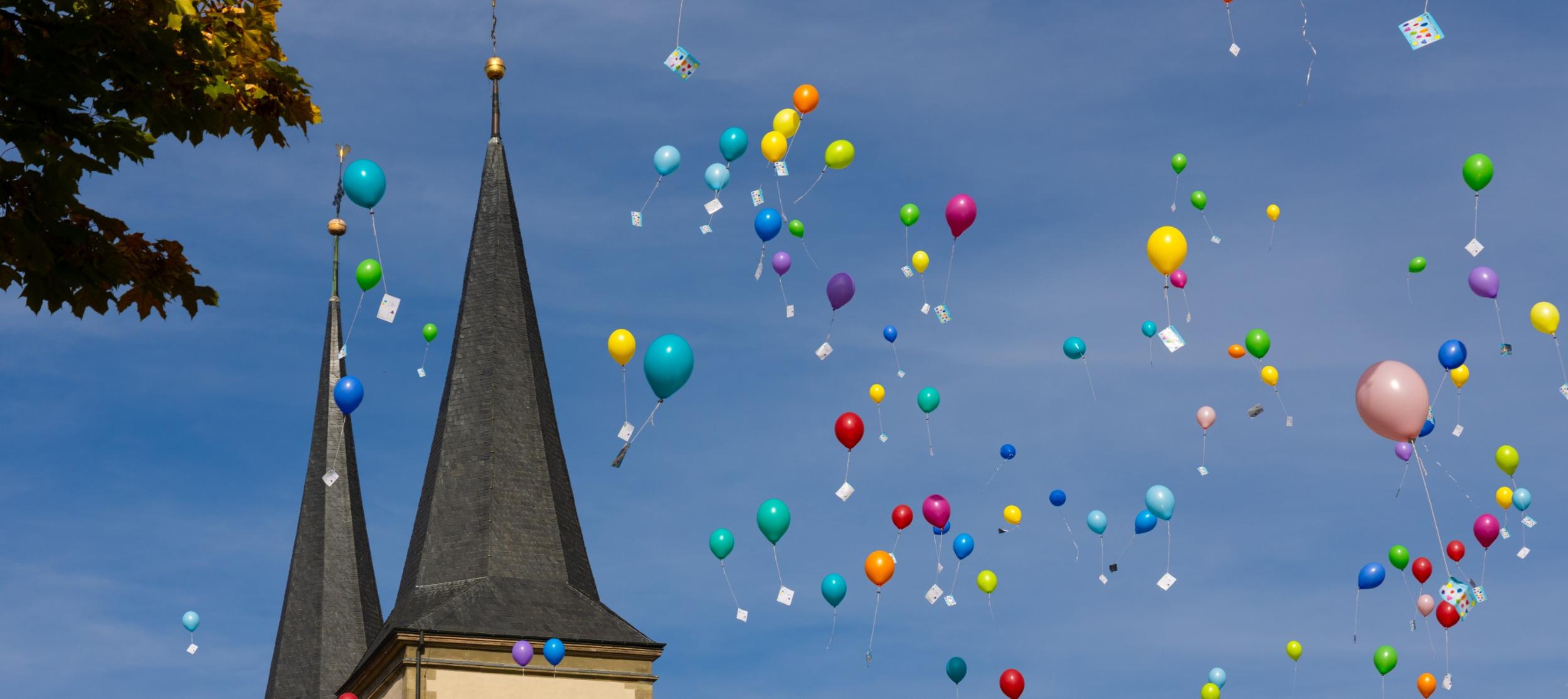 Bild mit aufsteigenden Luftballons vor zwei Kirchtürmen